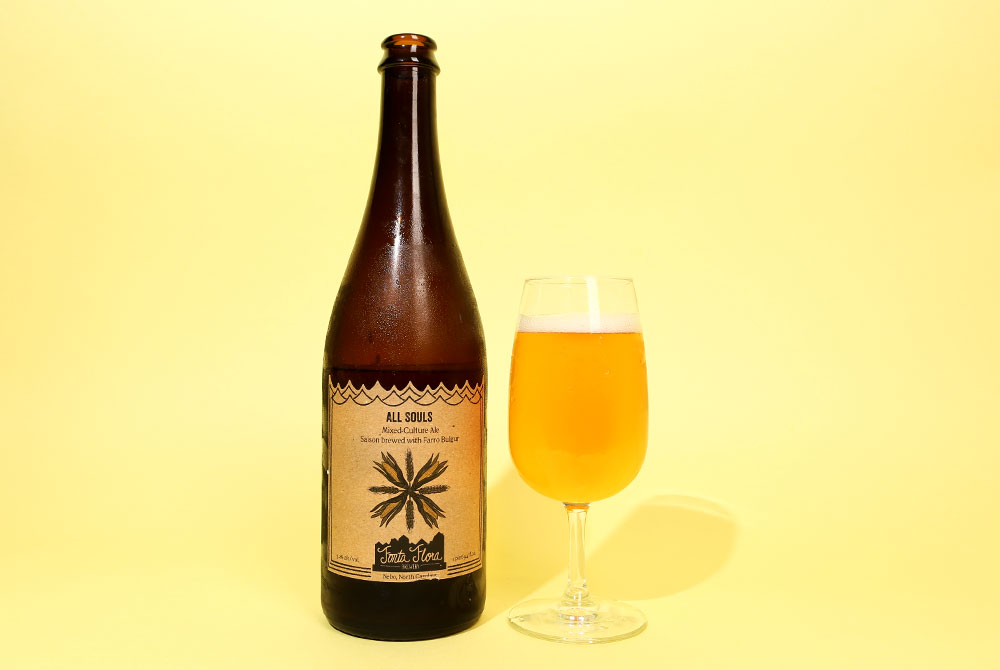 A saison beer in a bottle and glass on a honey yellow background